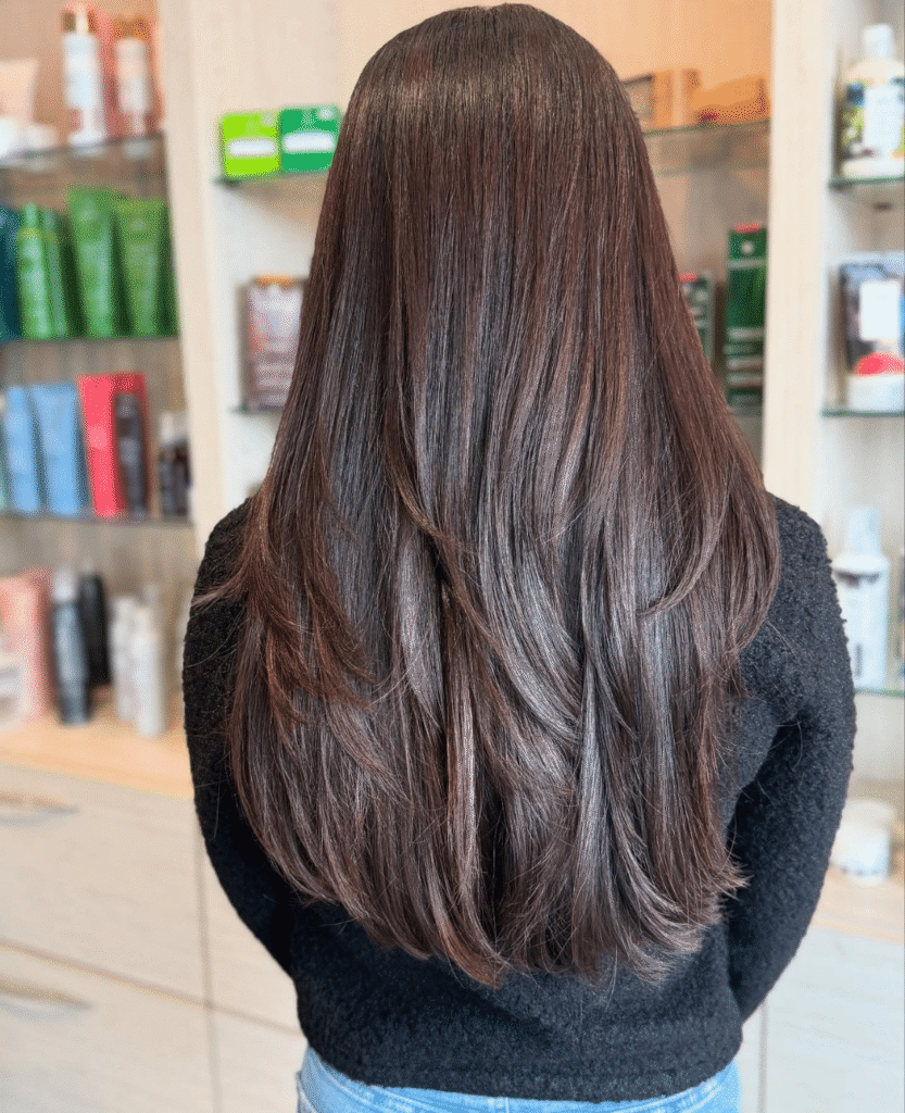 A woman showcases freshly styled, glossy brown hair with soft layers, reflecting the expert haircare and professional salon-quality results provided at Spitale Laser Spa Salon.