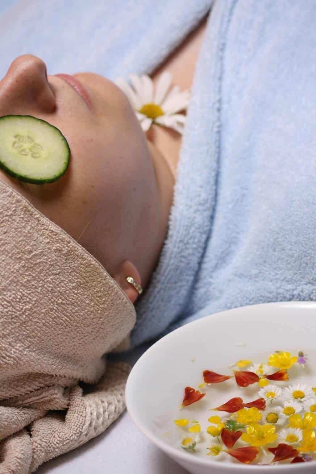 A woman relaxes during a rejuvenating facial treatment with cucumber slices on her eyes, wrapped in a soft towel and robe, representing the calming and revitalizing spa experience at Spitale Laser Spa Salon. Facials in Rochester.