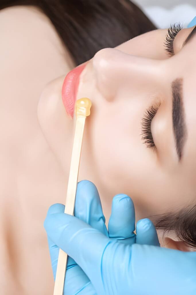 A professional esthetician applies warm wax above a client’s lip during a facial waxing session, demonstrating precision, hygiene, and expert care at a modern laser spa salon.